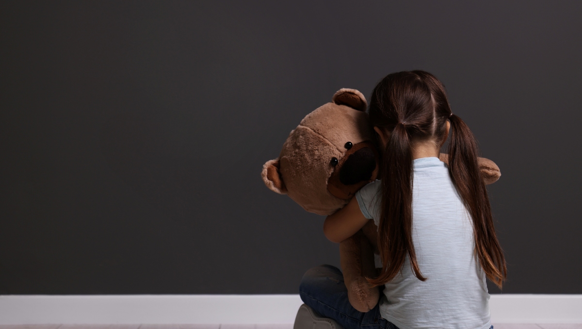 upset child sitting on floor hugging teddy bear