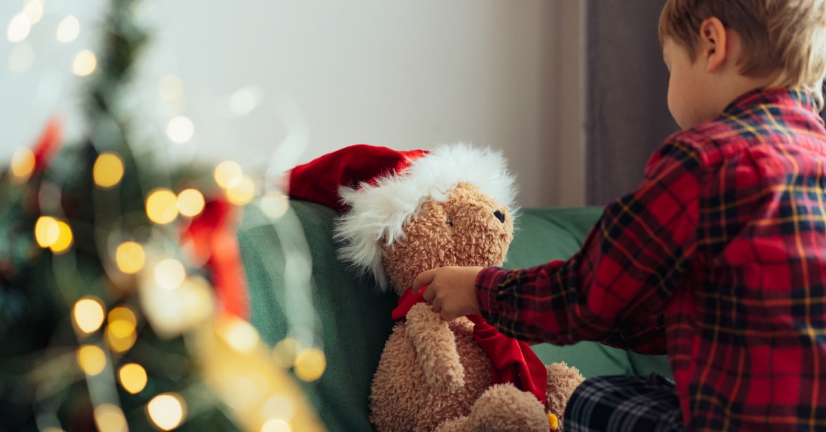 teddy bear sitting on green couch with boy and christmas tree