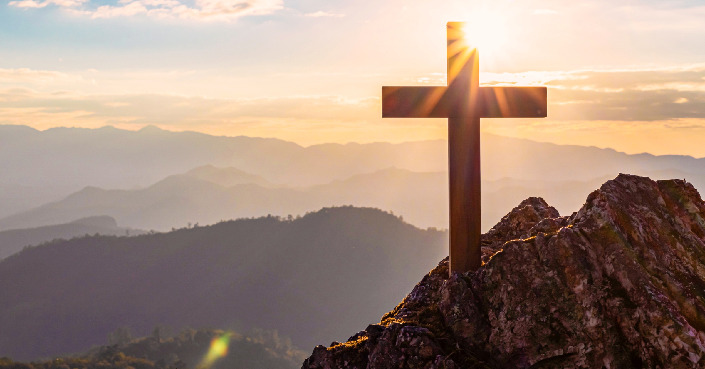 cross symbolizing resurrection on top of mountains with sun shining